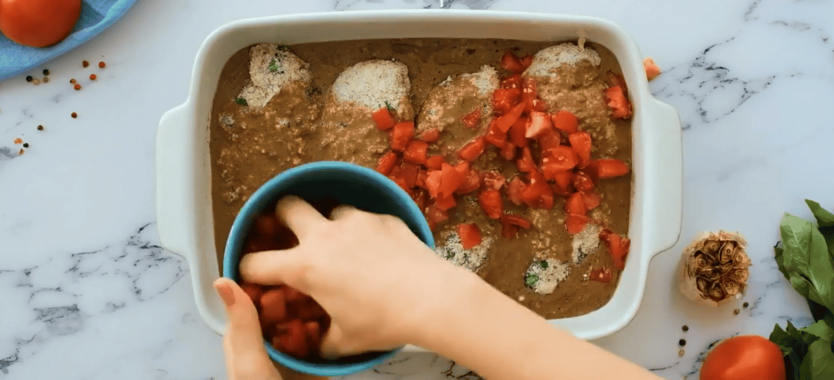 Covering the chicken with diced tomatoes.
