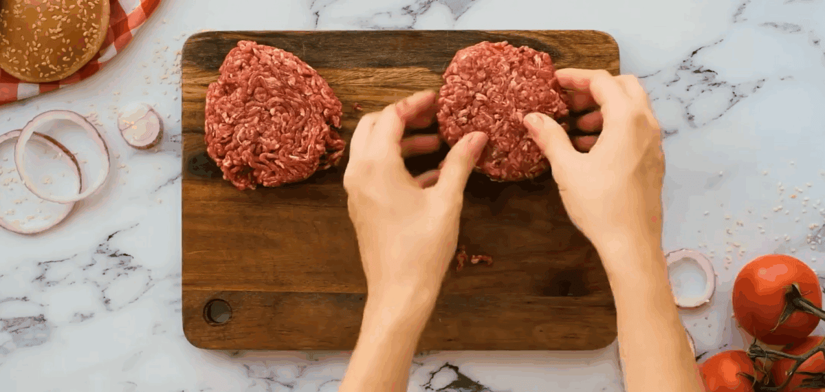 Shaping the ground beef into patties and placing them on a wooden cutting board.