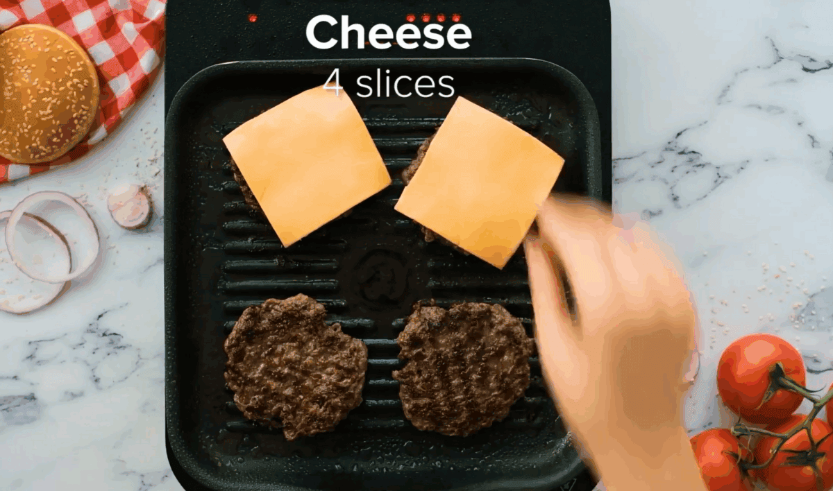 Placing a slice of cheese on each burger.