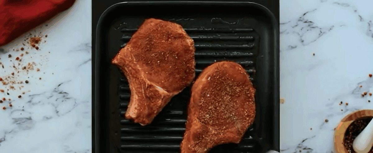 Two seasoned pork chops cooking on a grill. 
