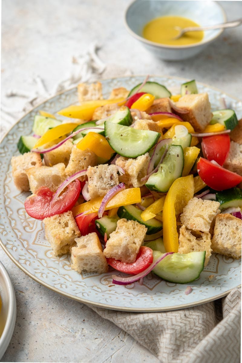 A close up of a panzanella salad on a plate with vinaigrette in the background