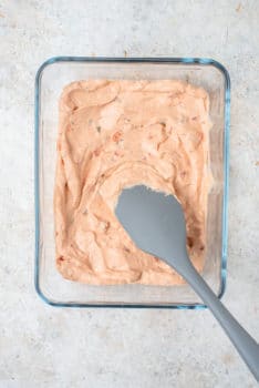 A spoon is being used to stir a bowl of icing for a layered taco dip.