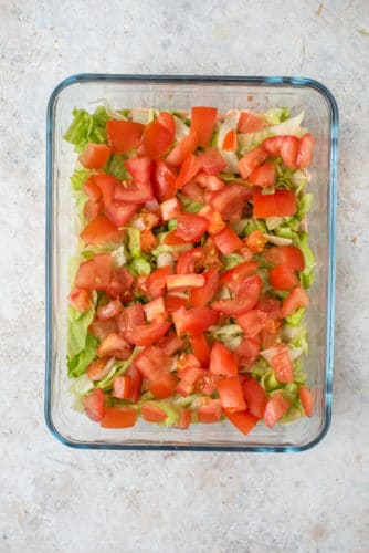 Layered taco dip with sliced tomatoes and lettuce in a glass dish.