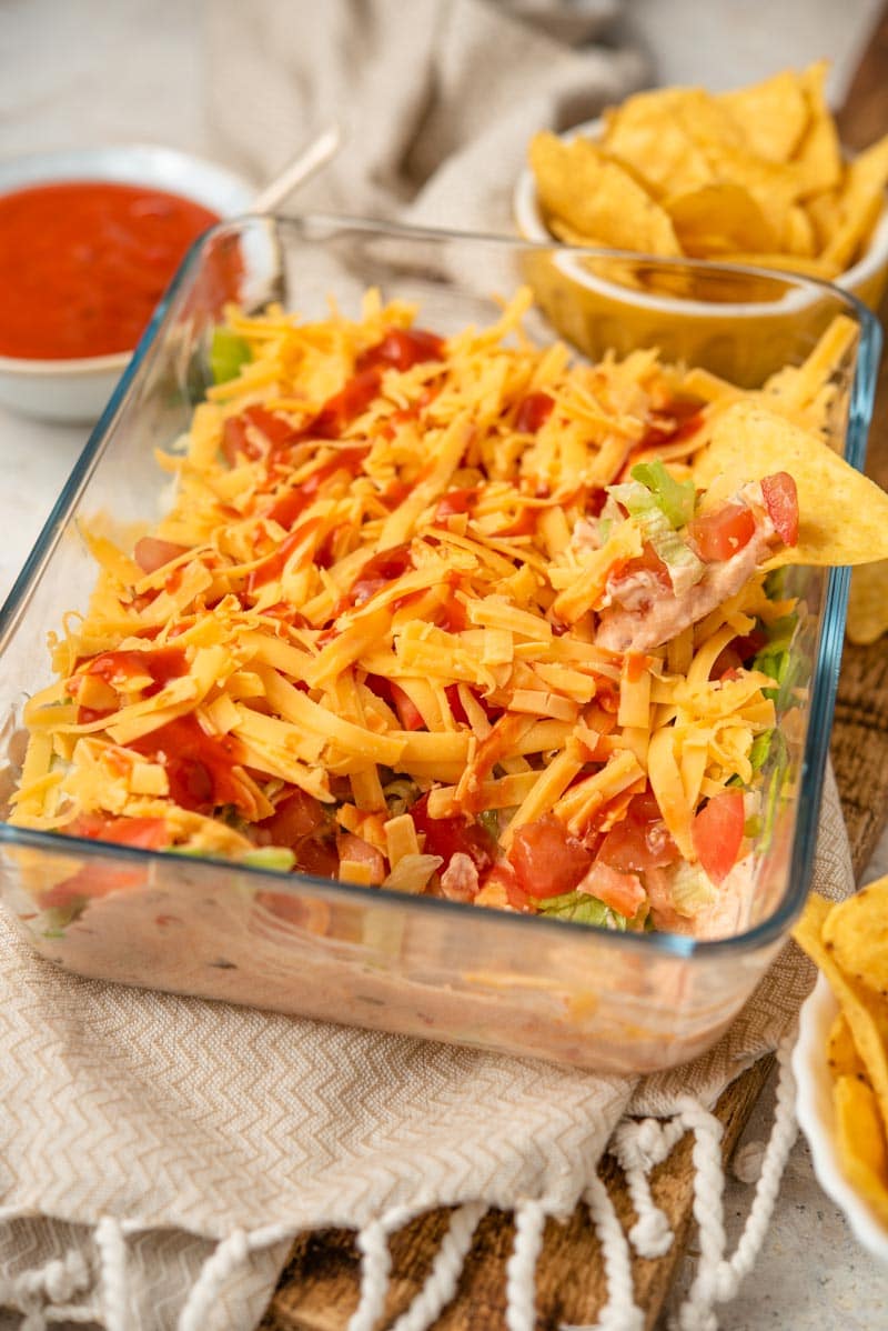 A close-up side shot of Layered Taco Dip with chips and taco sauce around it.