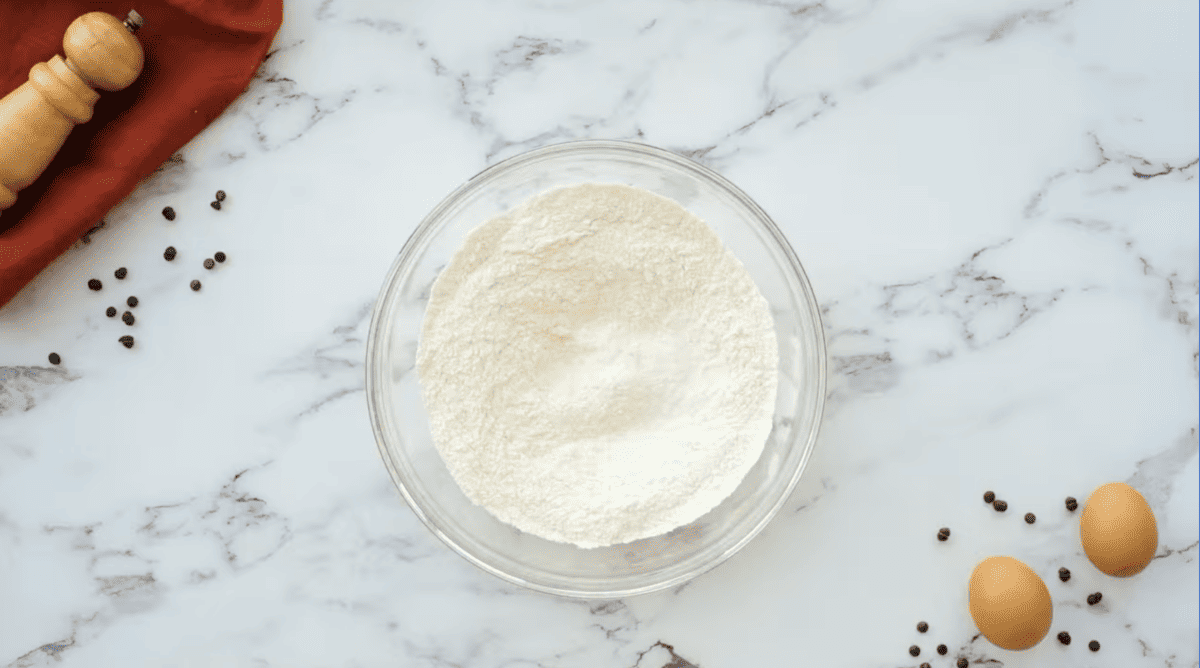 A bowl of flour and eggs on a marble table ready to make delicious Chocolate Chip Pancakes.