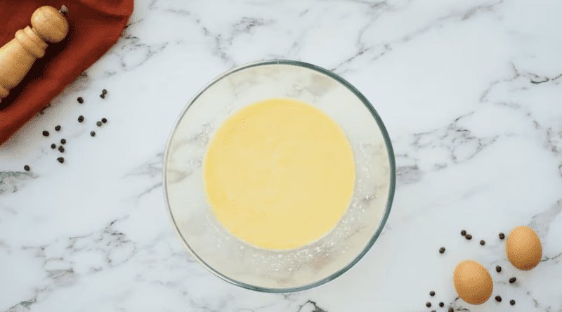 A bowl of egg yolks and spices mixed for the preparation of Chocolate Chip Pancakes, sitting on a sleek marble table.