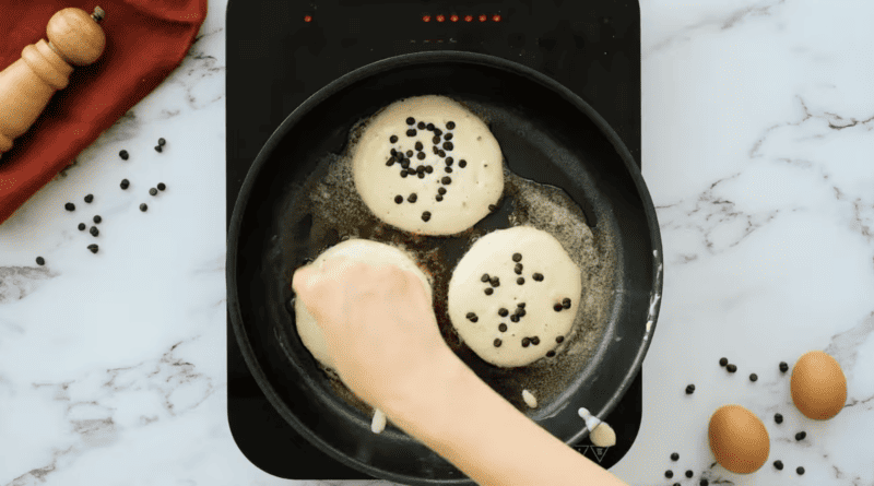 A person is frying chocolate chip pancakes in a pan.