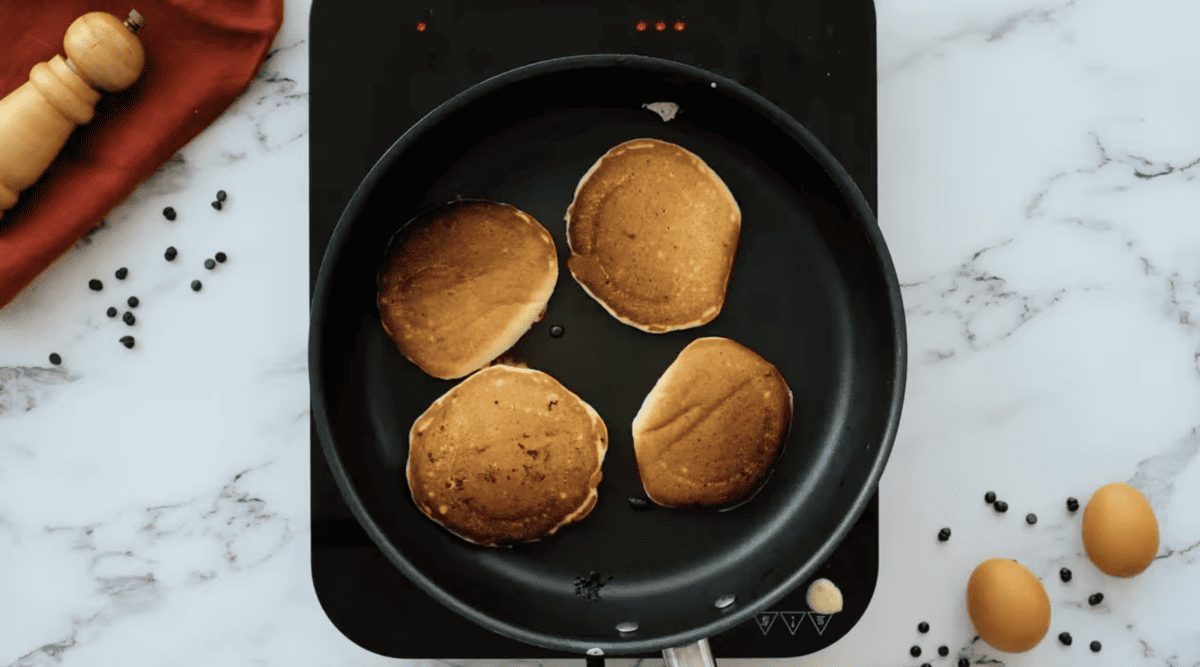 Chocolate chip pancakes are being cooked in a pan on a marble countertop.