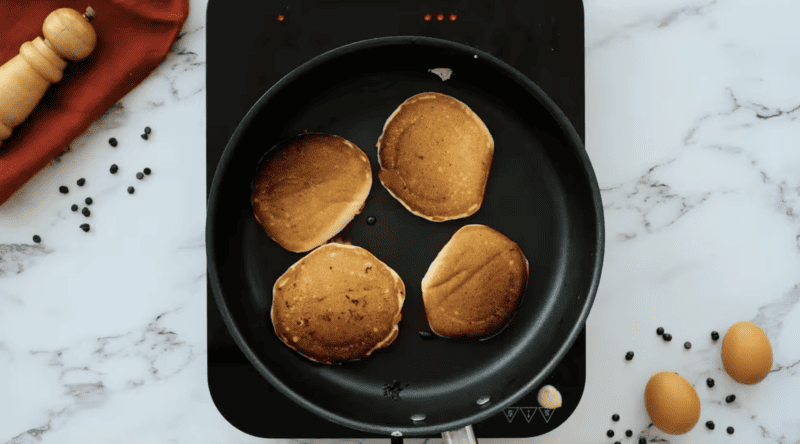 Chocolate chip pancakes are being cooked in a pan on a marble countertop.