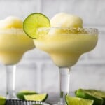 two frozen margarita glasses surrounded by sliced limes