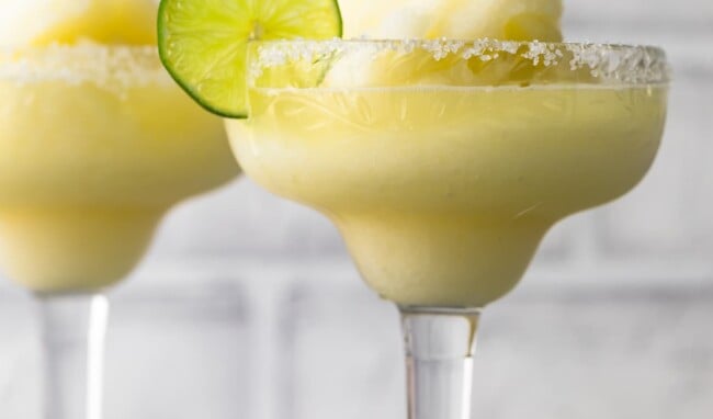 two frozen margarita glasses surrounded by sliced limes