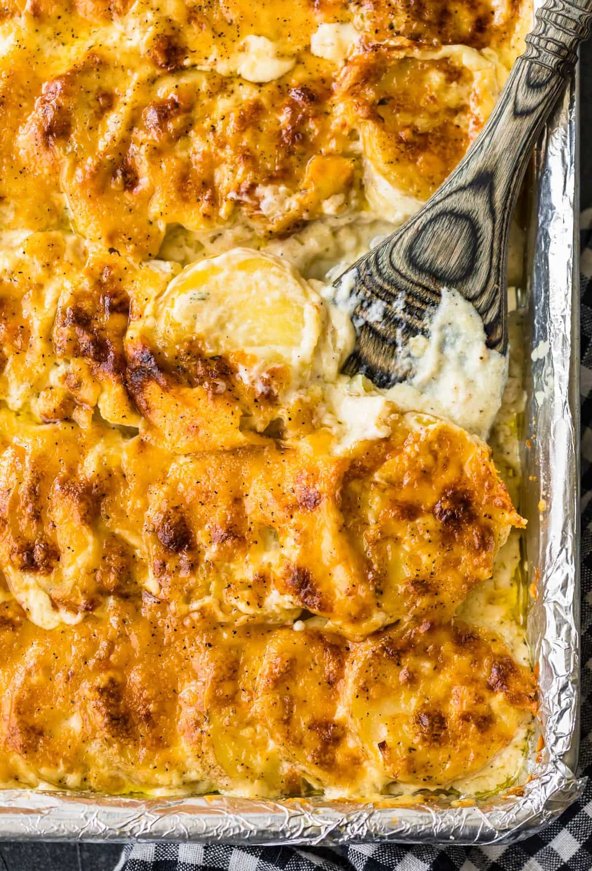 Sheet pan scalloped potatoes with a wooden spoon in them