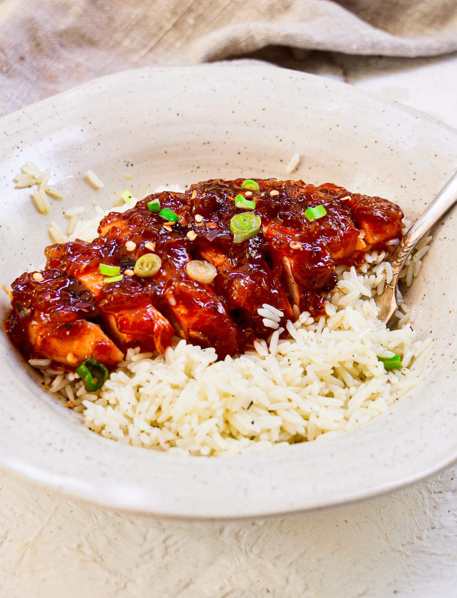 A sliced apricot chicken breast on a bed of rice in a white bowl.