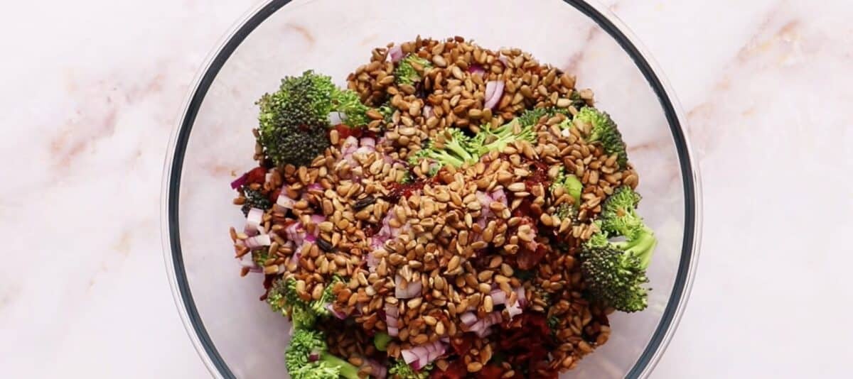 Combining the ingredients to make broccoli salad in a glass bowl.
