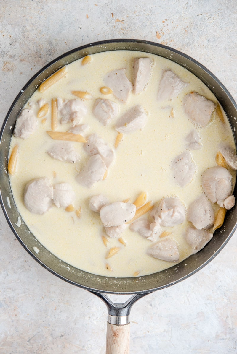 Chicken, pasta and cream in a pan for making one pot chicken alfredo