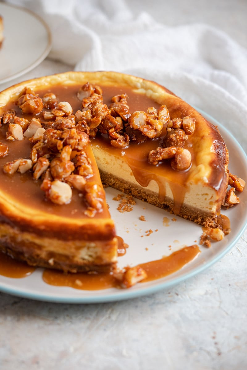 A caramel cheesecake on a plate with lots of caramel sauce and nuts