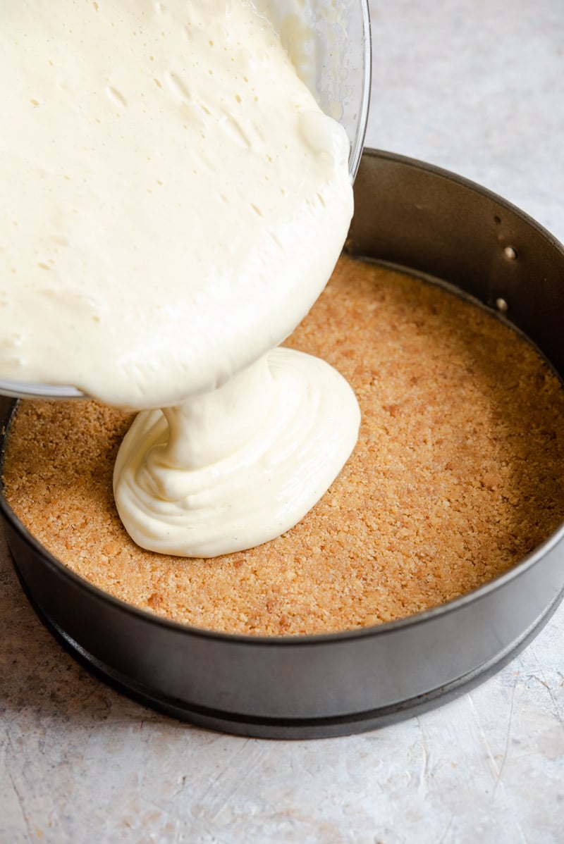 Pouring batter on a cheesecake base to make caramel cheesecake