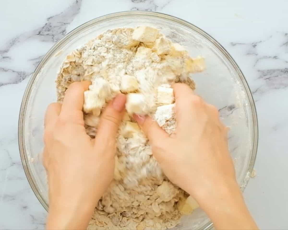 A pair of hands blending the oat and flour topping.