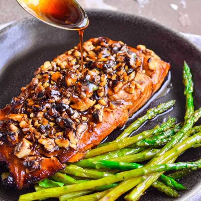 salmon and asparagus in skillet with glaze being spooned on it