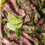 top shot of carne asada steak with sliced lime and cilantro