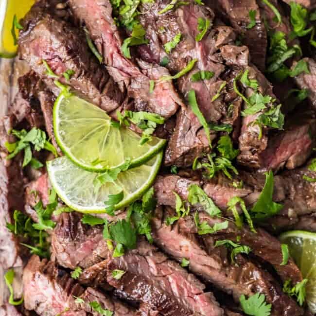 top shot of carne asada steak with sliced lime and cilantro