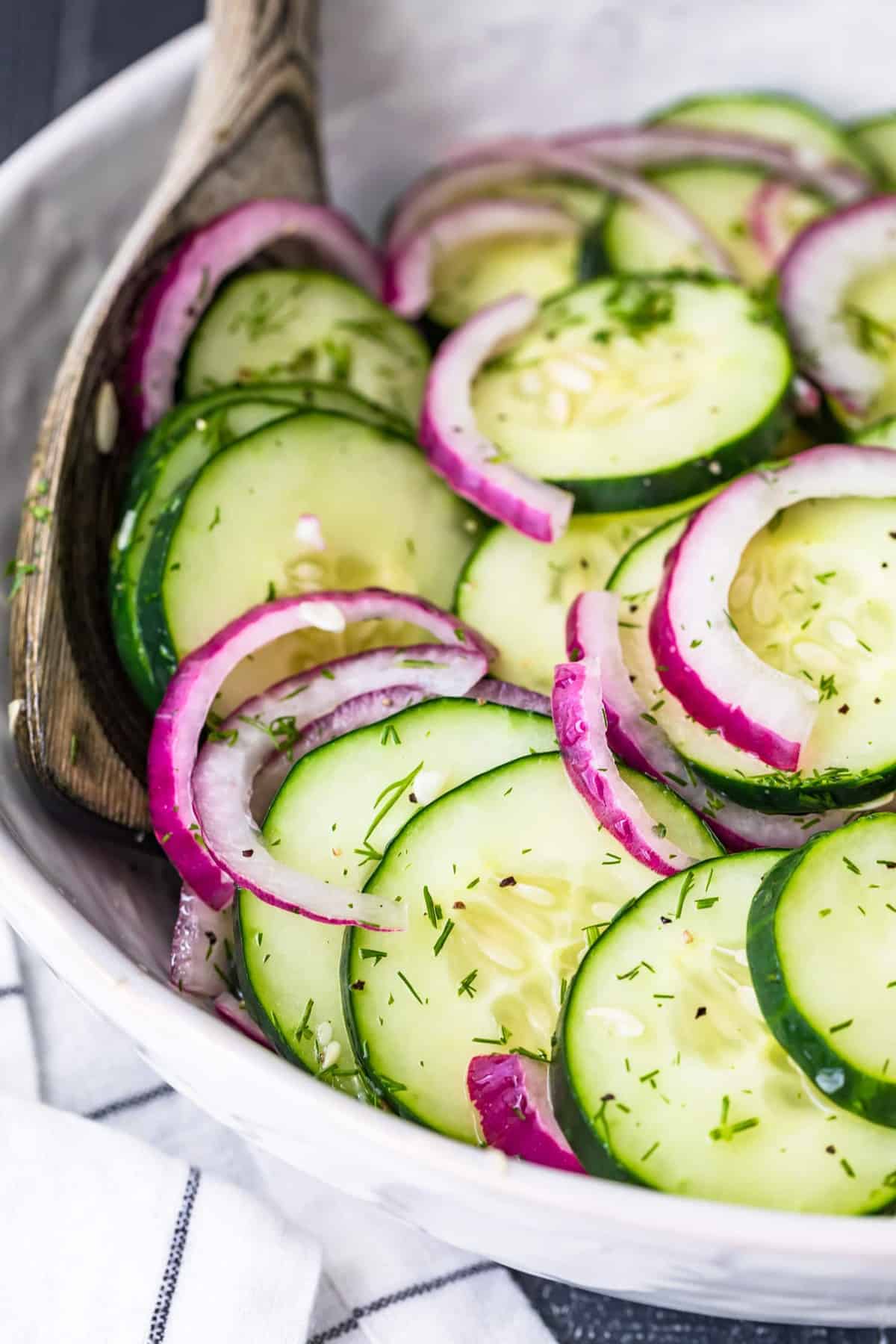 Close up of a wooden spoon in a cucumber salad