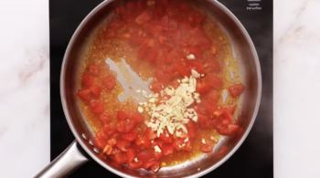 minced garlic added to tomatoes simmering in a pan.
