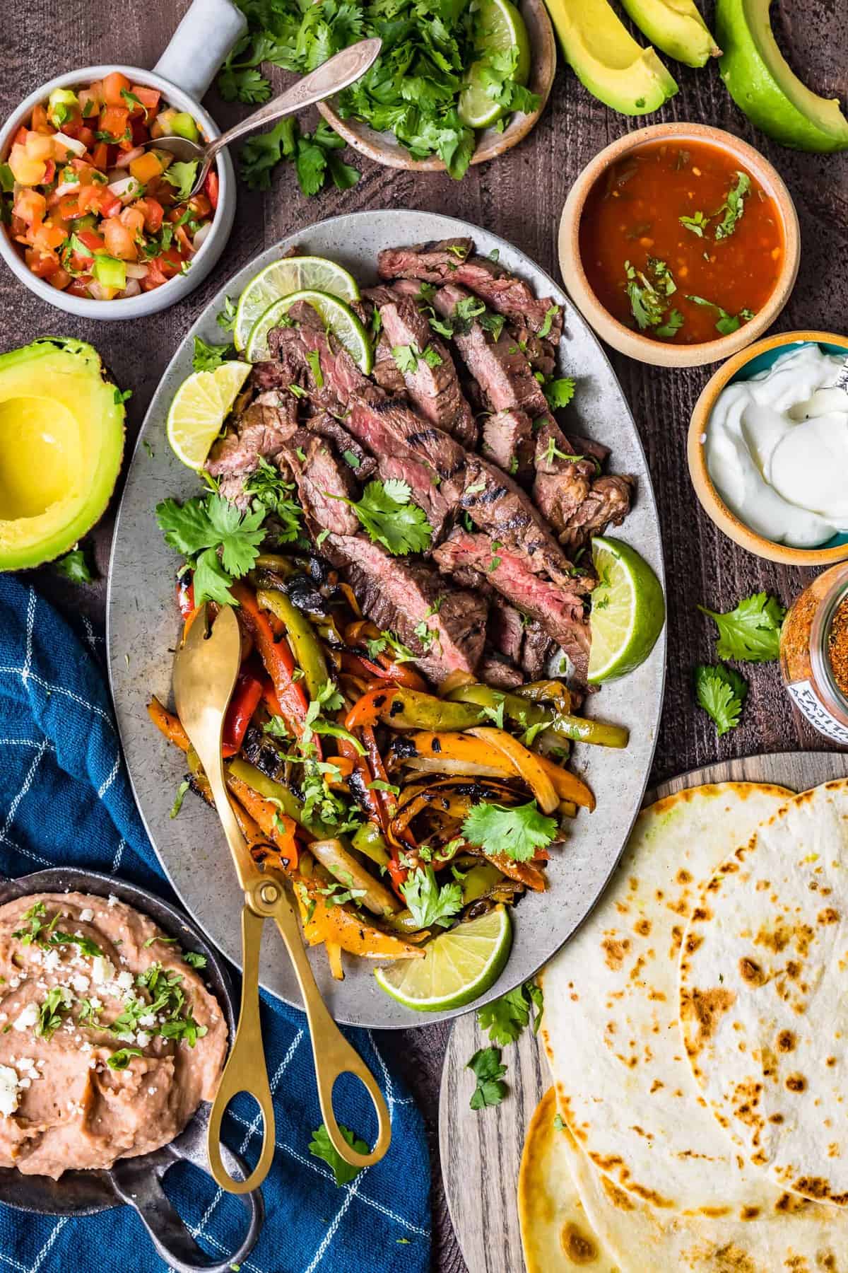 Steak fajitas on a serving plate next to sides and toppings