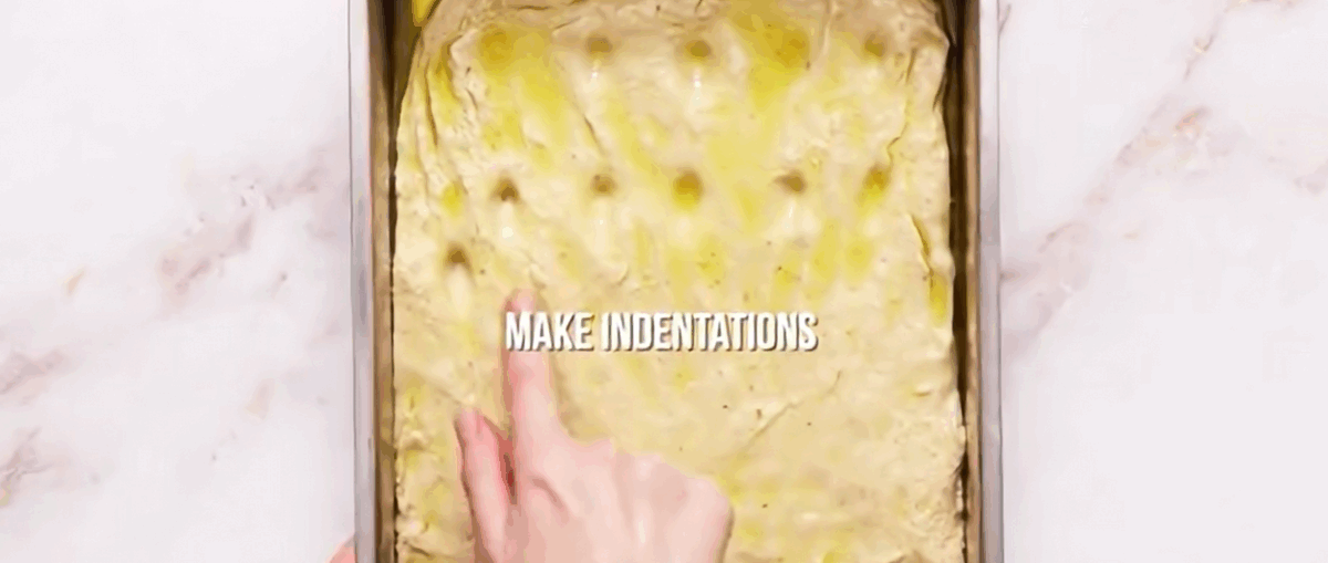 Focaccia dough in the greased pan with indentations.