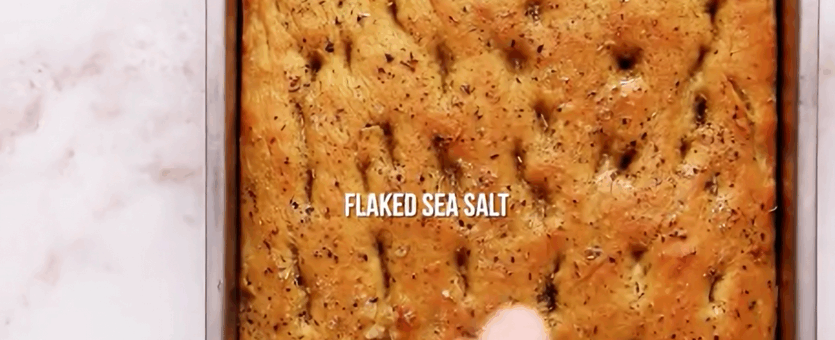Partially baked bread being sprinkled with flaked sea salt. 
