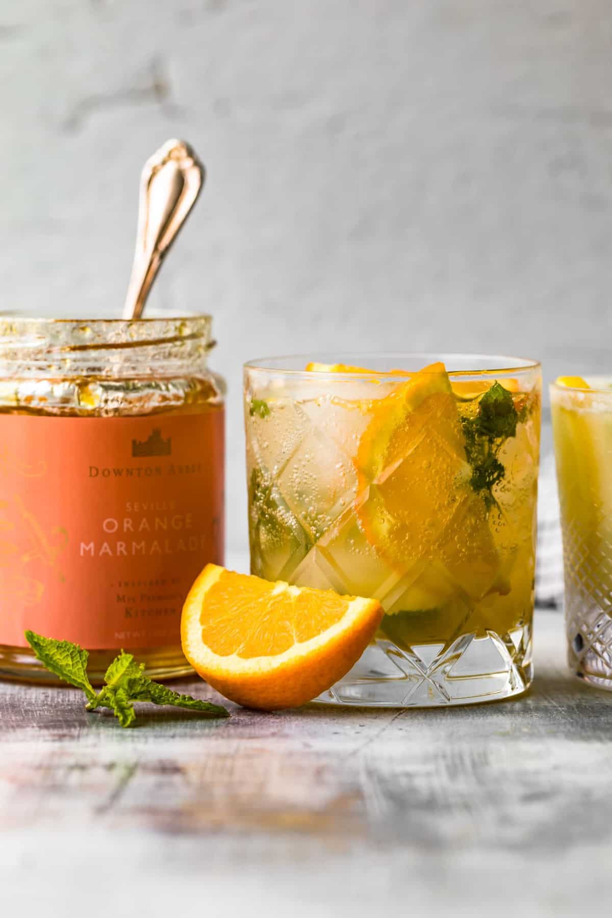 orange marmalade in a jar next to a cocktail on a table with a sliced orange