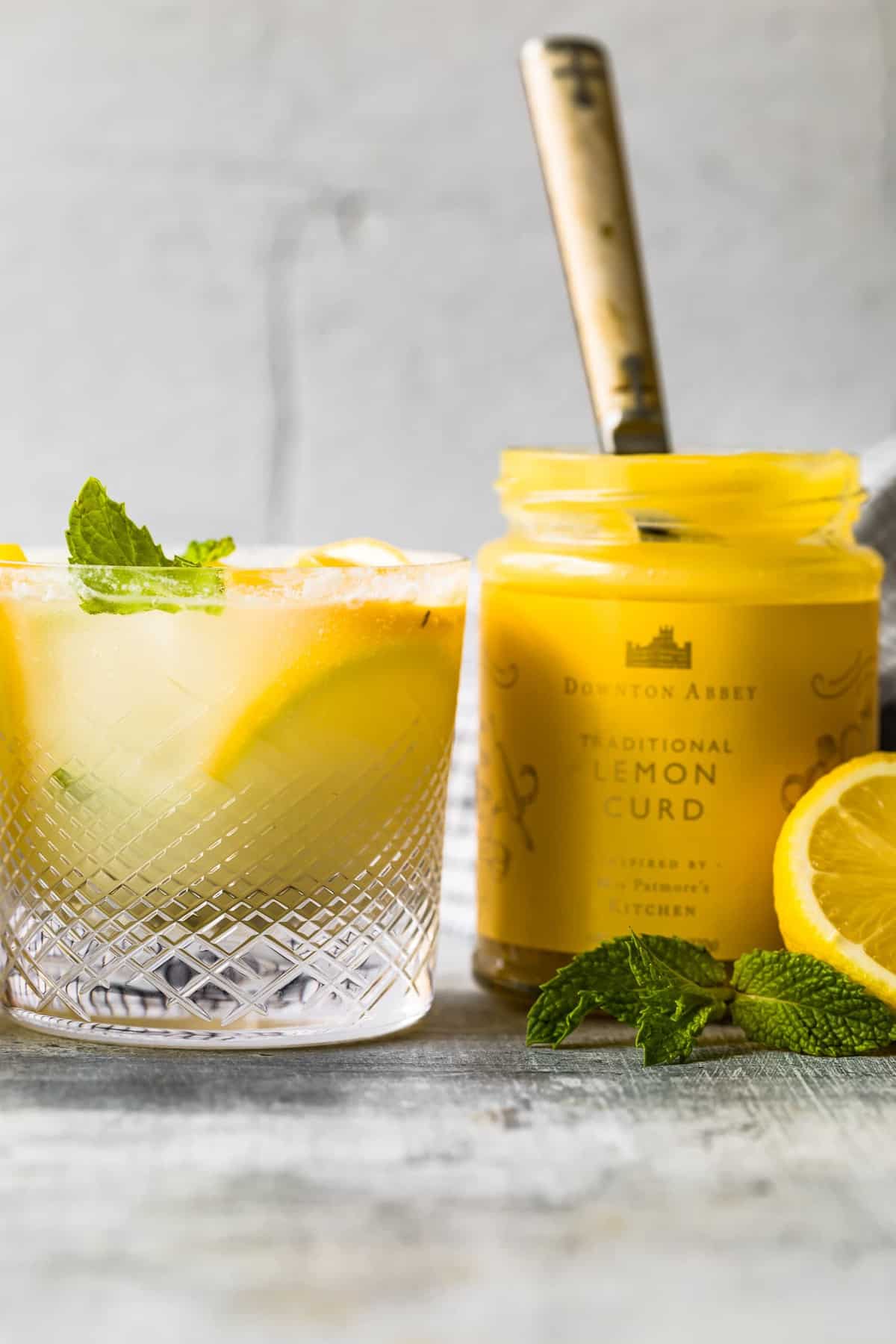 close up shot of traditional lemon curd in a jar next to a cocktail