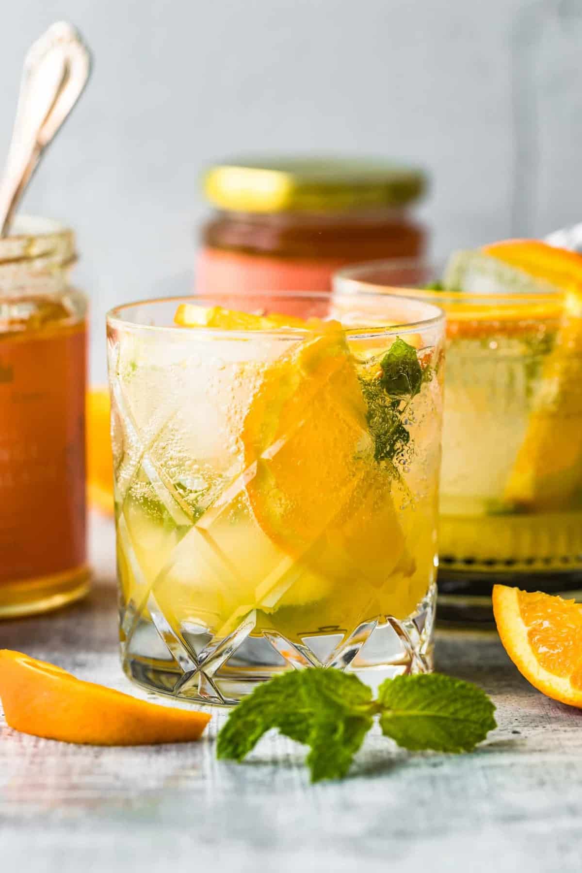 citrus smash cocktail on a table with sliced oranges and mint leaves