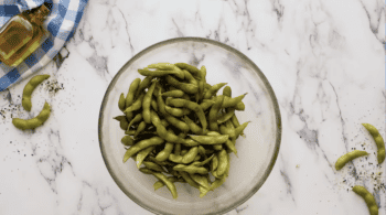 A delightful bowl of edamame, made from soybeans, sits elegantly on a sleek marble table.