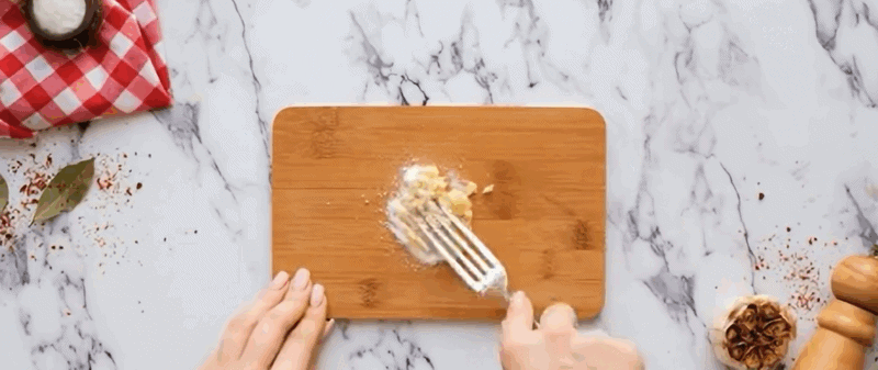 Preparing garlic paste on a wooden cutting board.
