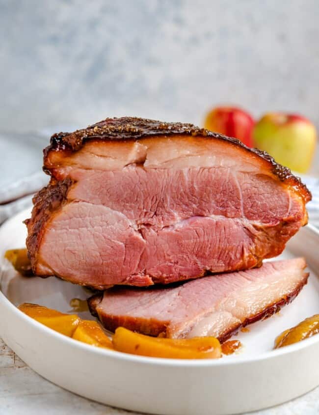 A side shot of a glazed ham with cooked apples