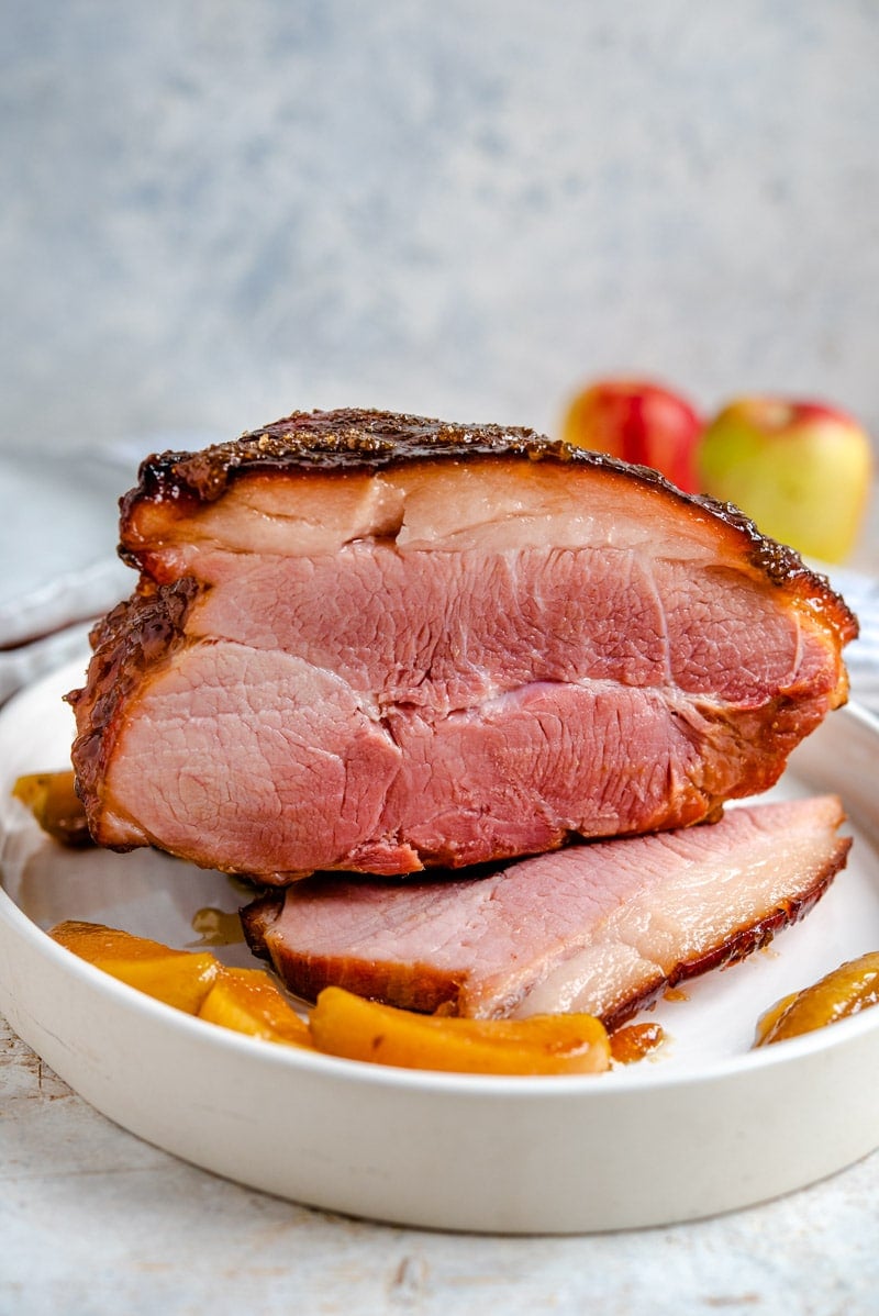 A side shot of a glazed ham with cooked apples