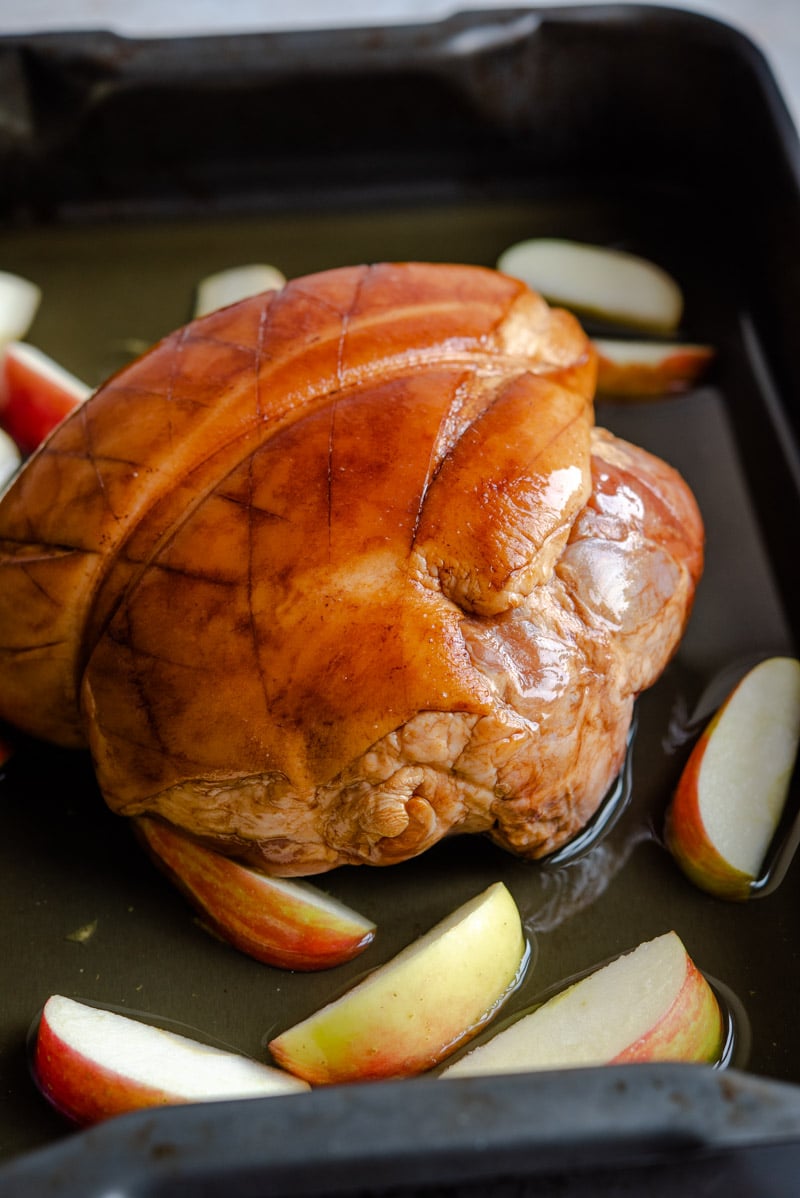 A ham in a baking tray with apples and juice