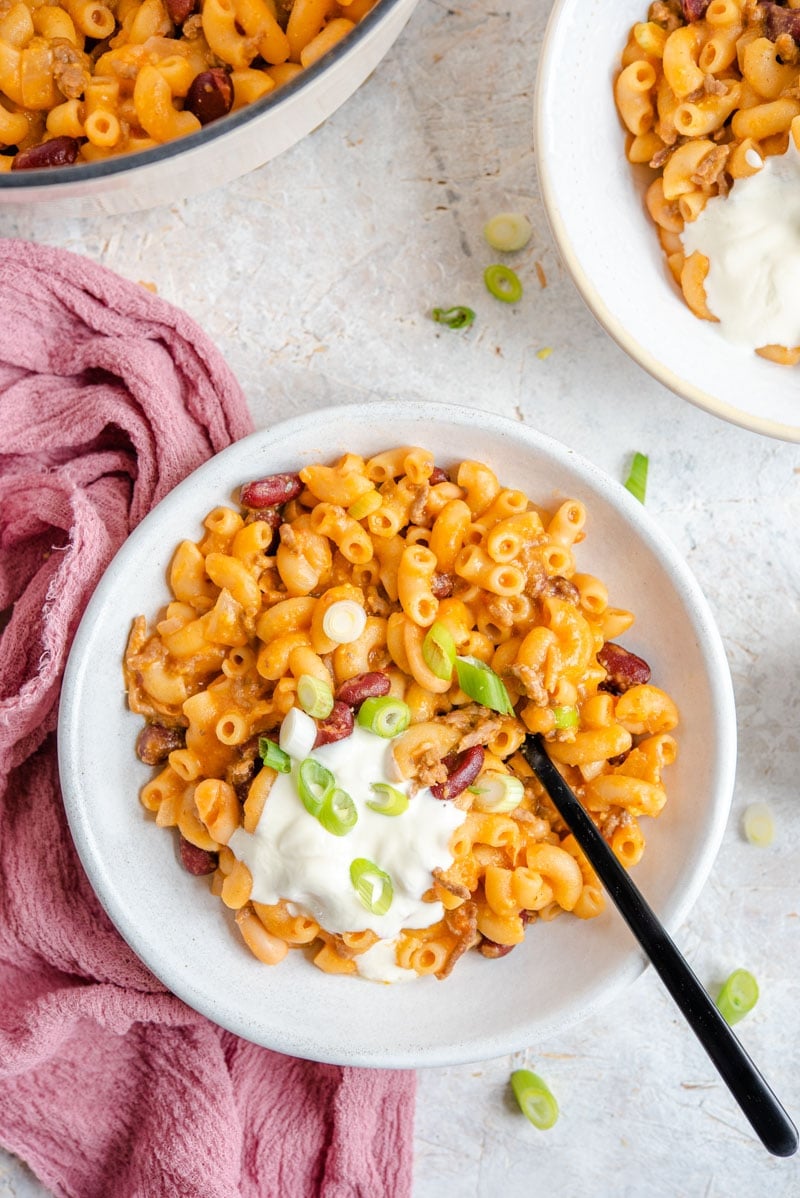 An overhead shot of Loaded Chili Mac and Cheese in a bowl, topped with sour cream and scallions.