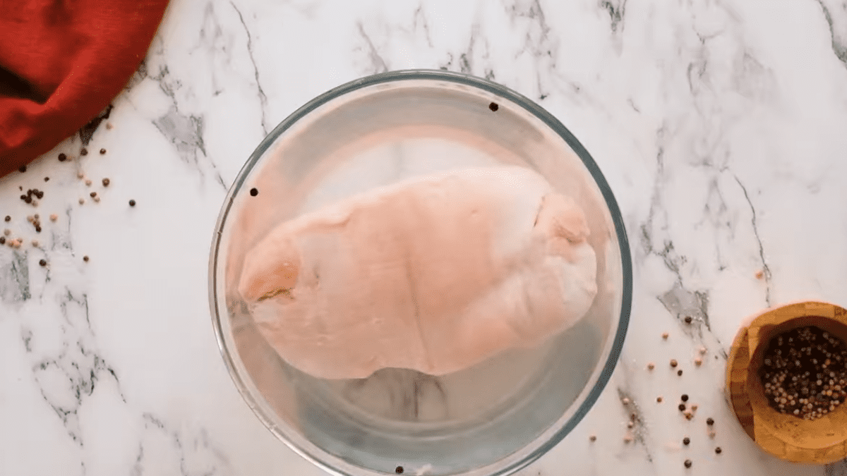 uncooked turkey breast submerged in brine in a glass bowl