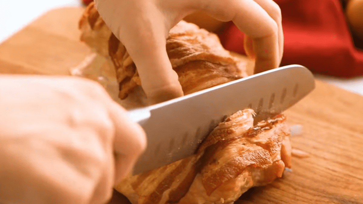 hands holding a chef's knife, slicing bacon wrapped turkey breast