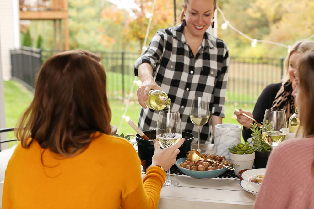 a woman pouring wine into another woman's wine glass sitting at a table outside