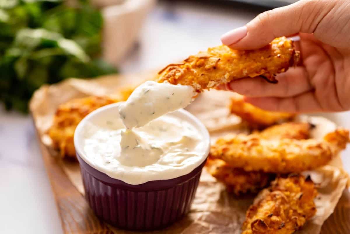 A chicken finger being dipped into a creamy sauce