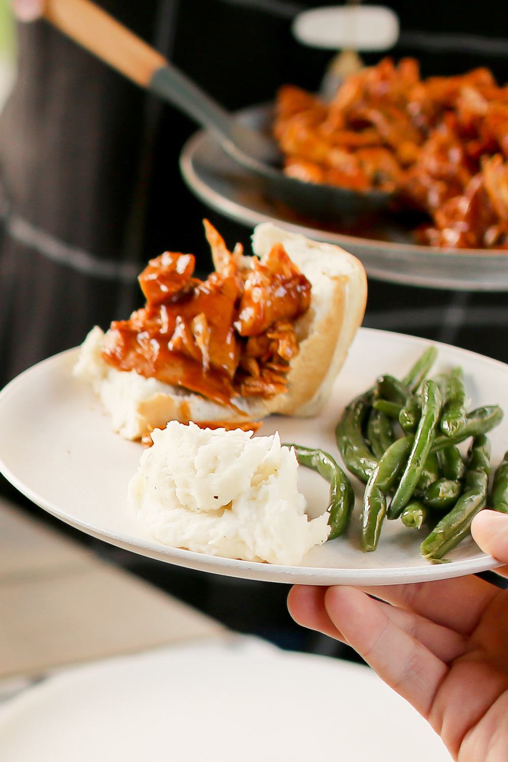 Close up view of a plate filled with green beans, mashed potatoes, and a bun with brisket