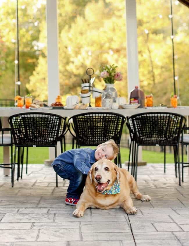 A young boy hugging a dog with a table behind them