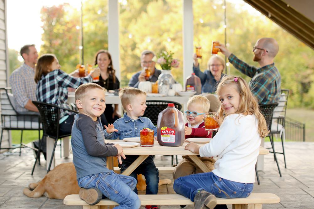 Kids sitting at a smaller table with a gallon of tea on the table and adults behind them