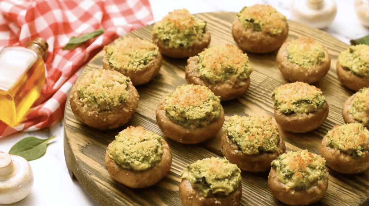 spinach stuffed mushrooms on a round wooden cutting board.