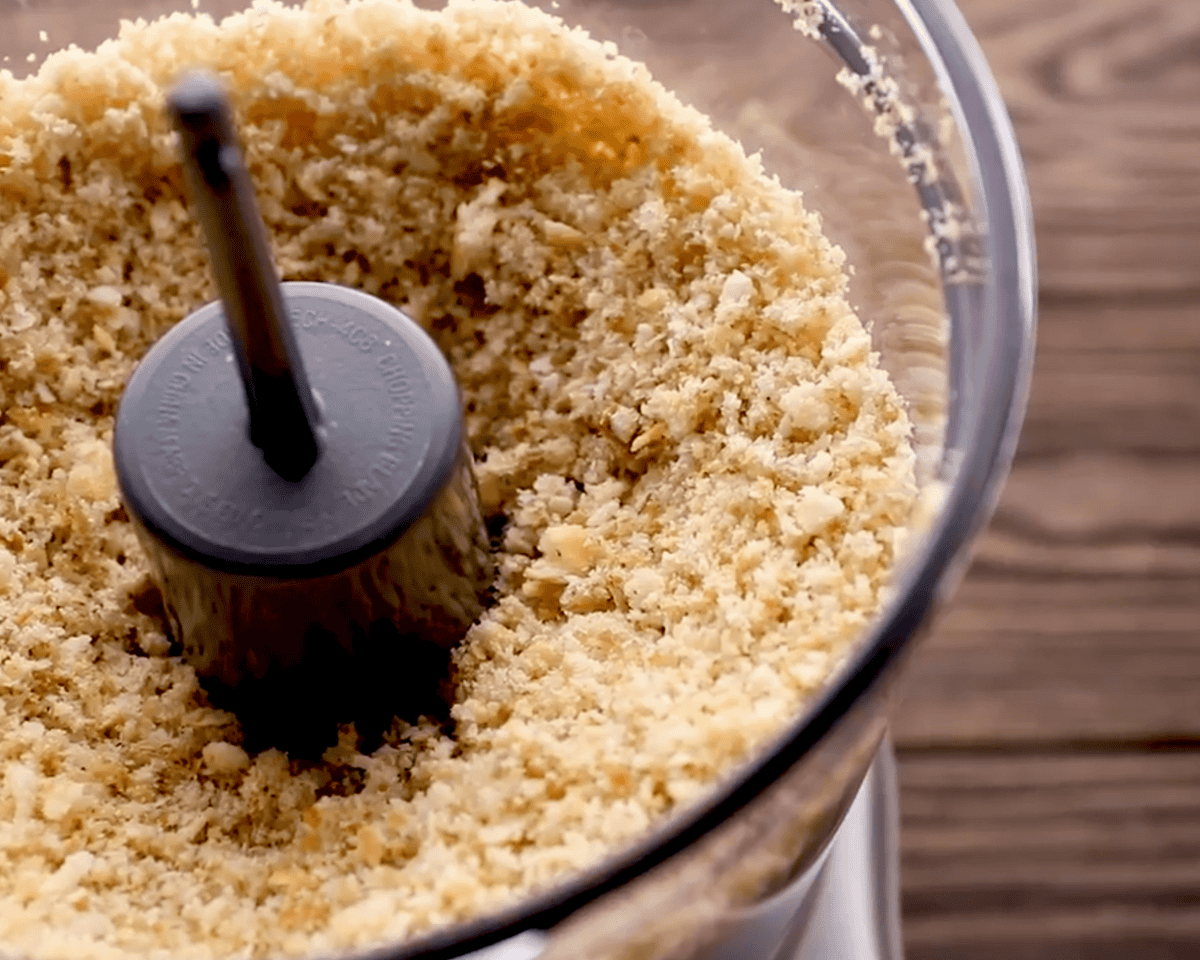 Close-up of Ritz crackers and sandwich bread blended into fine golden crumbs in a food processor.