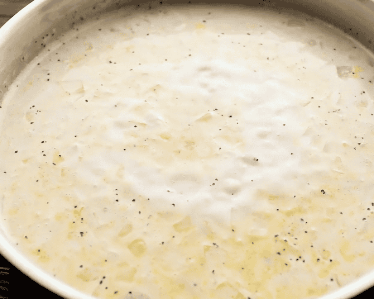 Creamy broth mixture simmering in the pan with seasonings and rice.