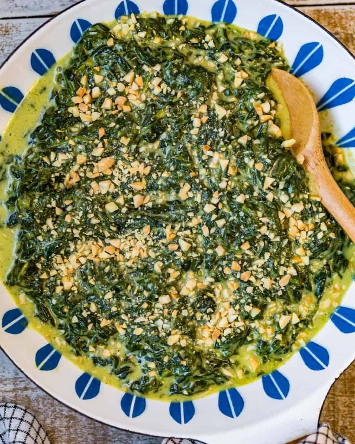 Creamed spinach with toasted almonds on a white and blue plate with a wooden spoon.
